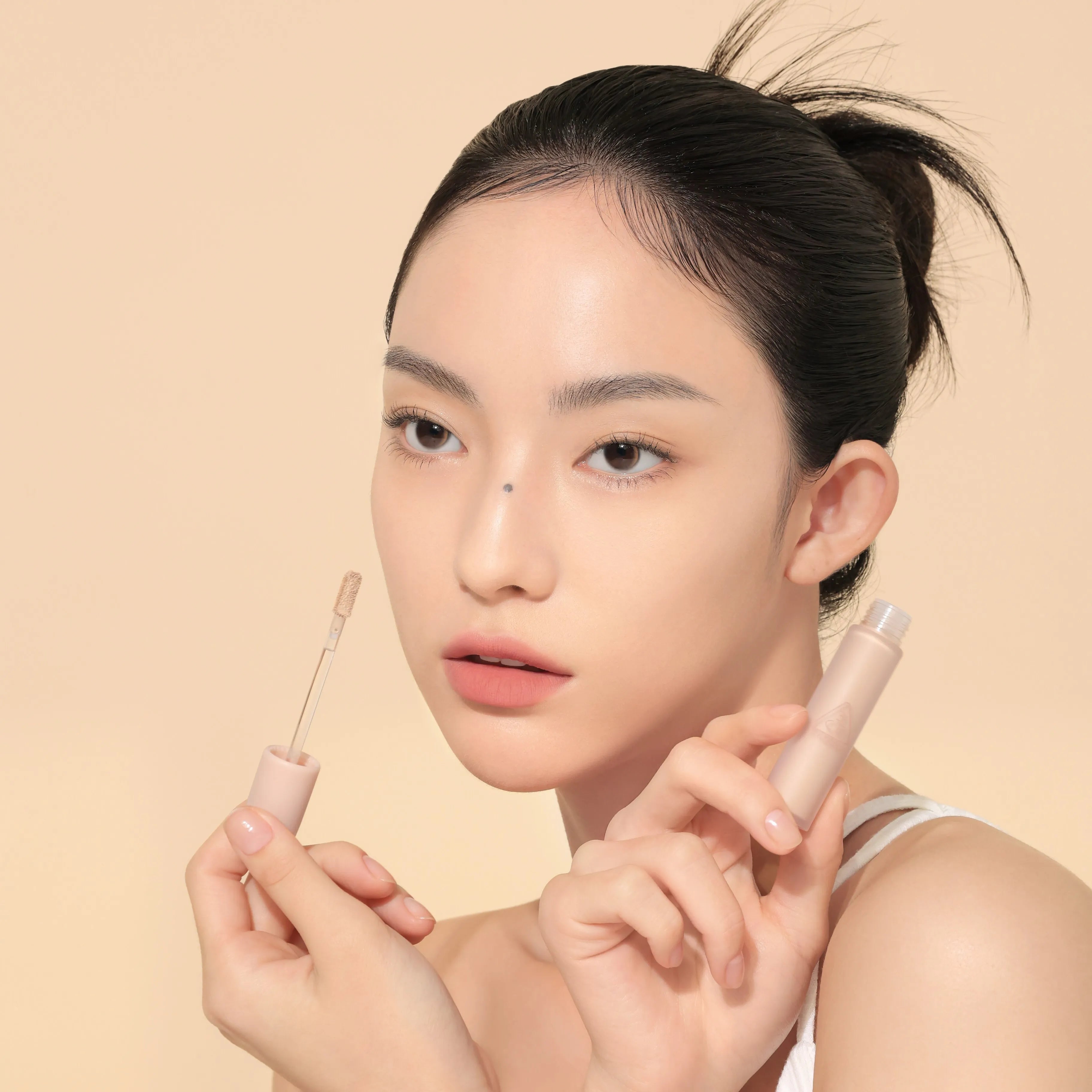 Portrait maquillage : 3CE Skin Fit Cover Liquid Concealer de 3CE, application sous les yeux sur fond beige.