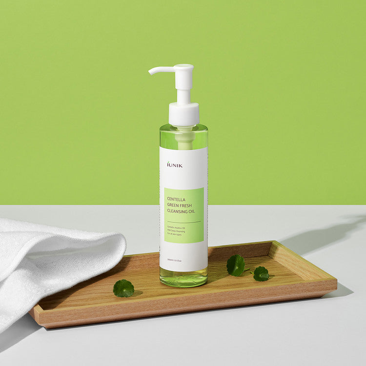 iUNIK Centella Green Fresh Cleansing Oil 200ml, flacon vert avec pompe sur plateau bois, serviette blanche, fond vert