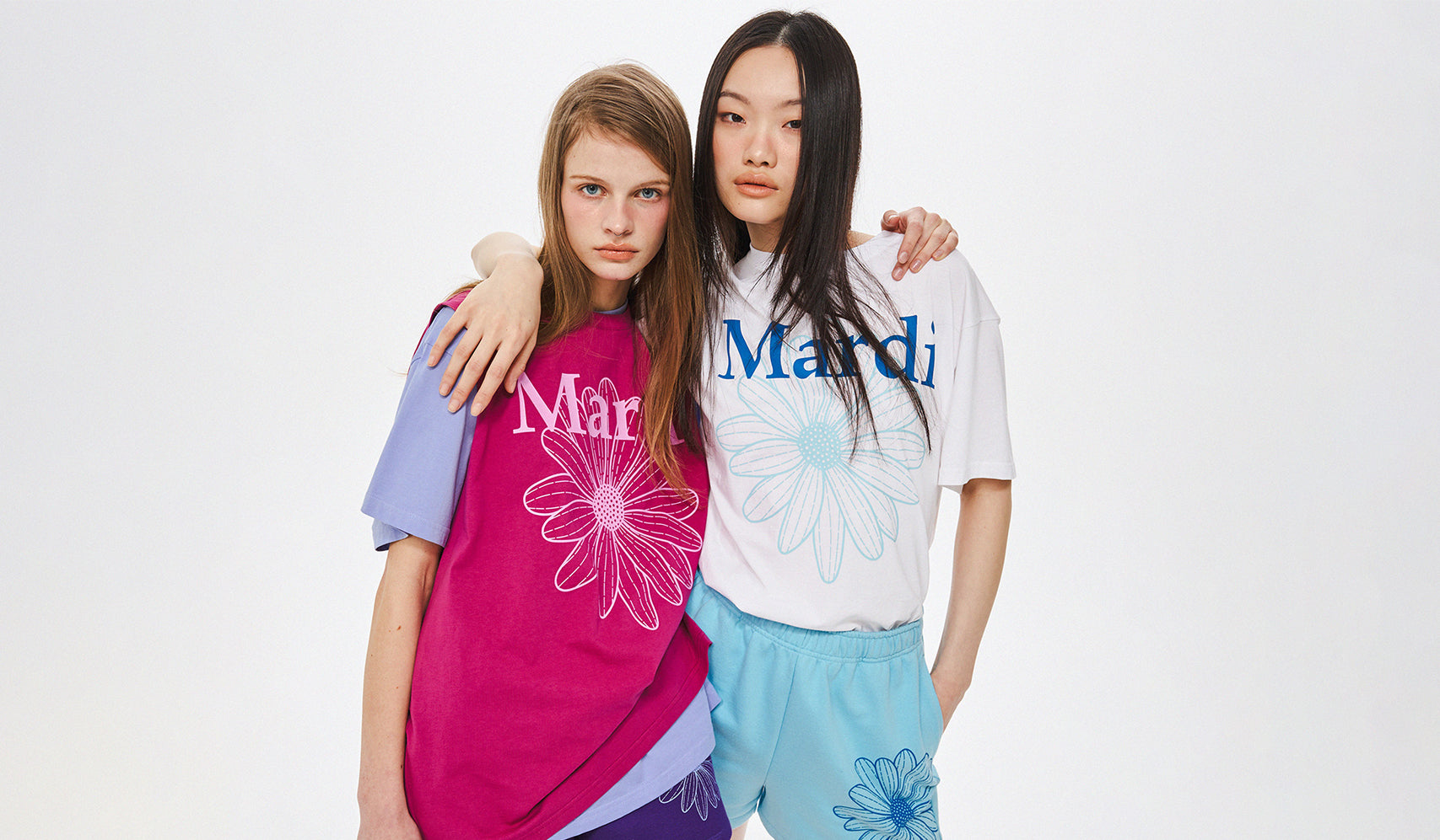 Two women posing in colorful fashion outfits with embroidered floral designs, studio portrait