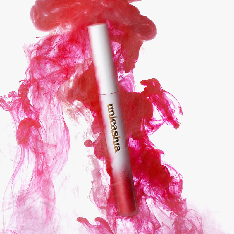 UNLEASHIA Luv Hug Velvet Tint de la marque UNLEASHIA, tube maquillage rouge sur fond blanc, fumée rose visuelle.