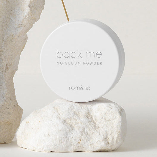 ROMAND White Rice No Sebum Powder, poudre visage de la marque rom&nd sur pierre blanche, décor minimaliste, fond crème.