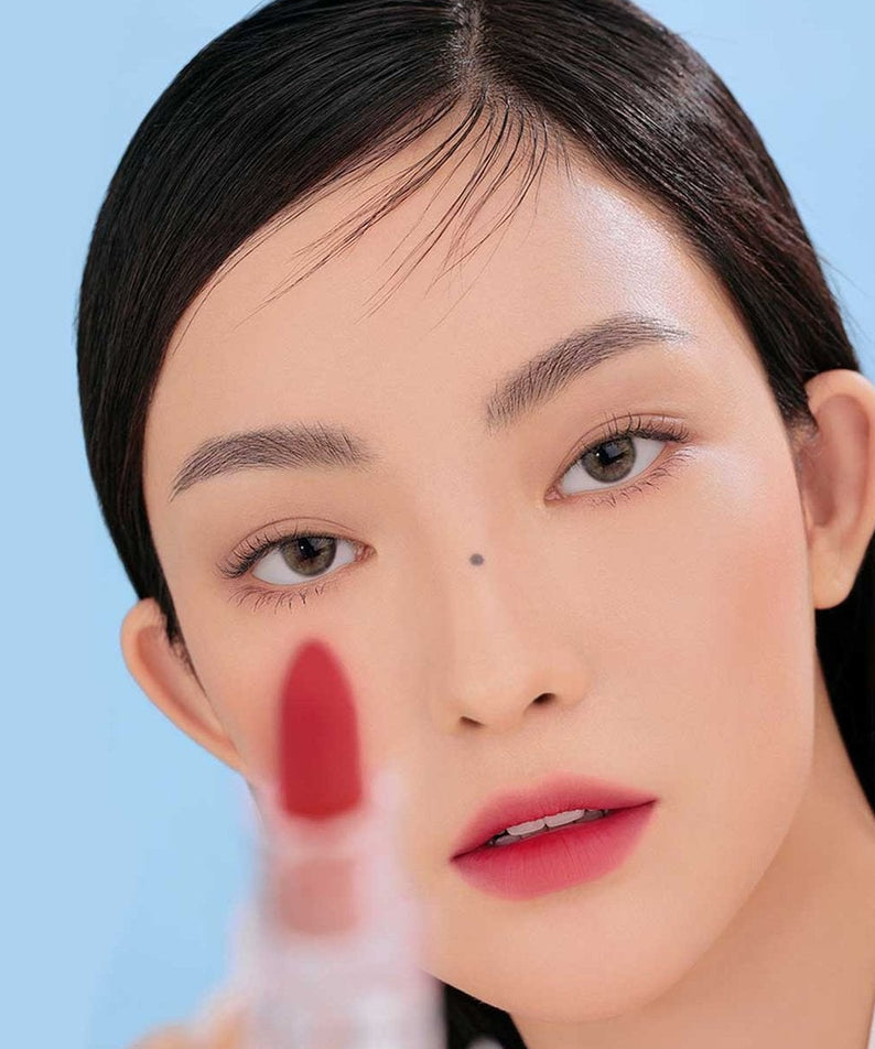 Maquillage : 3CE Soft Matte Lipstick sur les lèvres, marque 3CE, portrait de femme sur fond bleu clair.