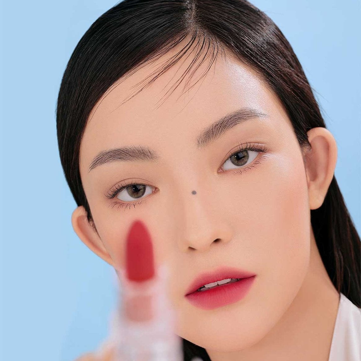 Maquillage : 3CE Soft Matte Lipstick sur les lèvres, marque 3CE, portrait de femme sur fond bleu clair.