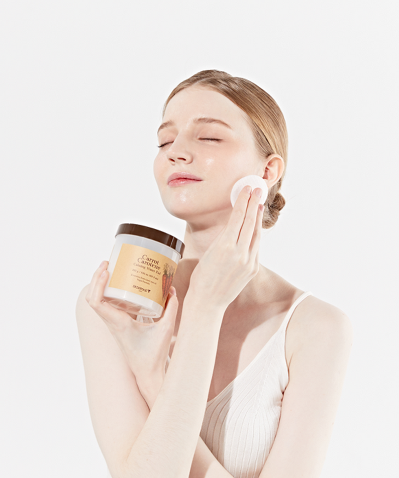 SKINFOOD Carrot Carotene Calming Water Pad de la marque SKINFOOD, visage hydraté appliquant un pad, contexte skincare.