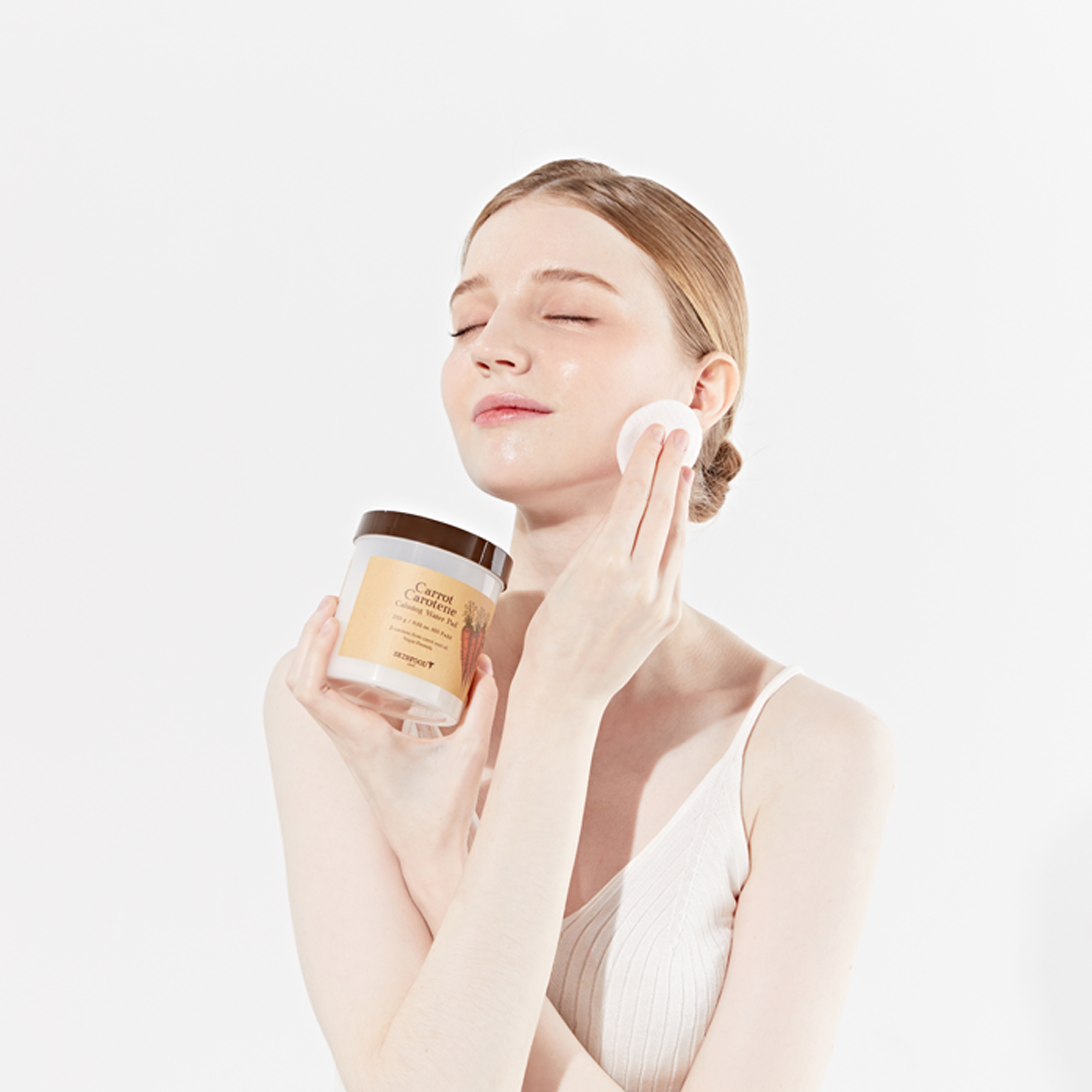 SKINFOOD Carrot Carotene Calming Water Pad de la marque SKINFOOD, visage hydraté appliquant un pad, contexte skincare.