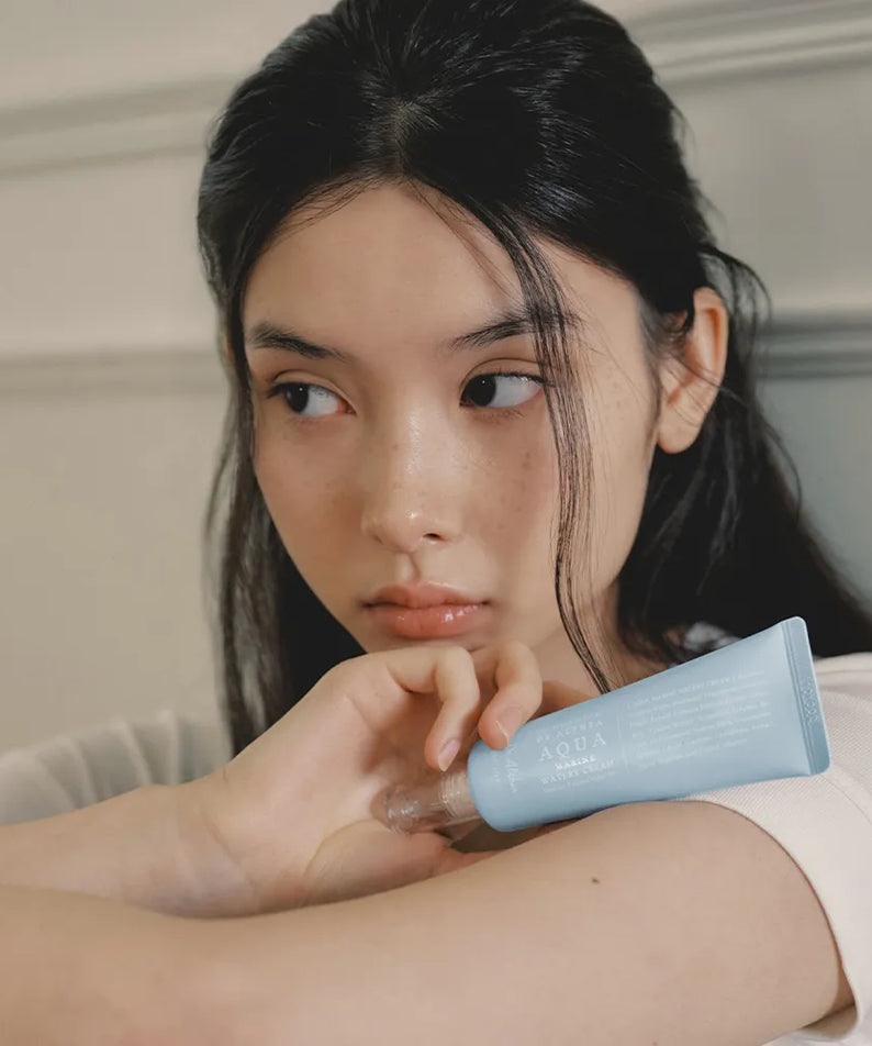 Femme tenant DR.ALTHEA Aqua Marine Watery Cream 50ml, crème hydratante visage en tube bleu.