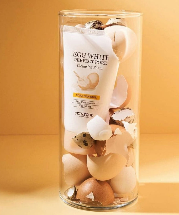SKINFOOD Egg White Perfect Pore Cleansing Foam 150ml, mousse nettoyante en tube, présentée avec coquilles d’œufs sur fond beige.