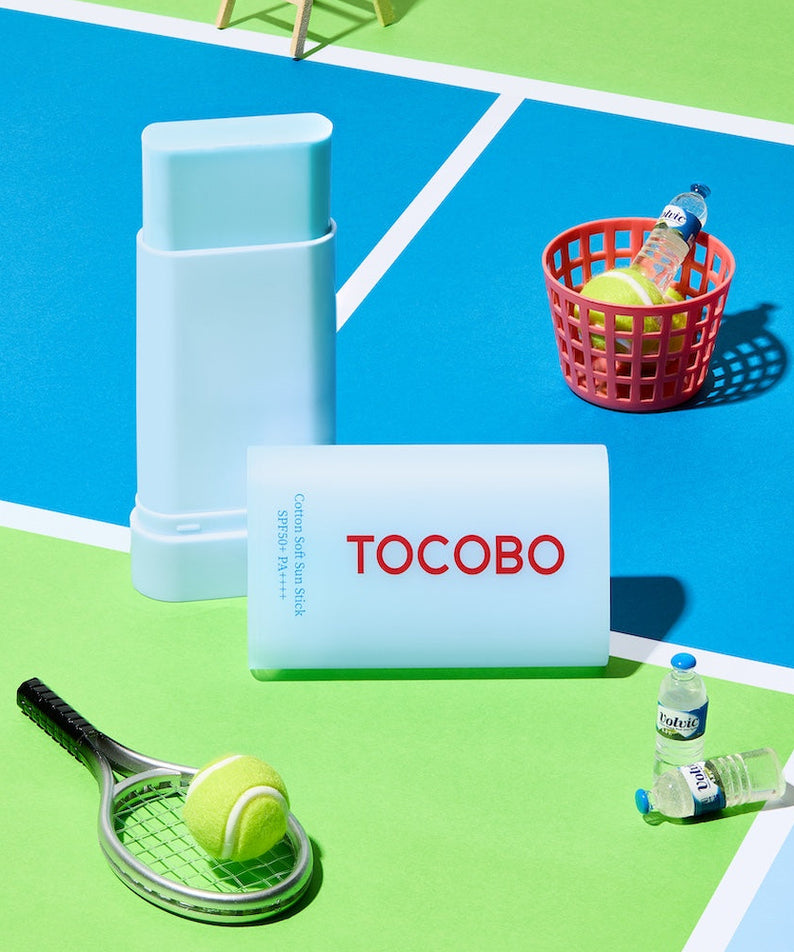 TOCOBO  Cotton Soft Sun Stick de la marque TOCOBO sur décor de plage coloré, stick solaire et accessoires