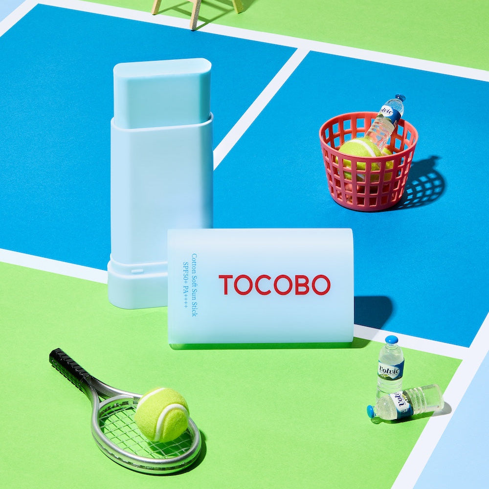 TOCOBO  Cotton Soft Sun Stick de la marque TOCOBO sur décor de plage coloré, stick solaire et accessoires