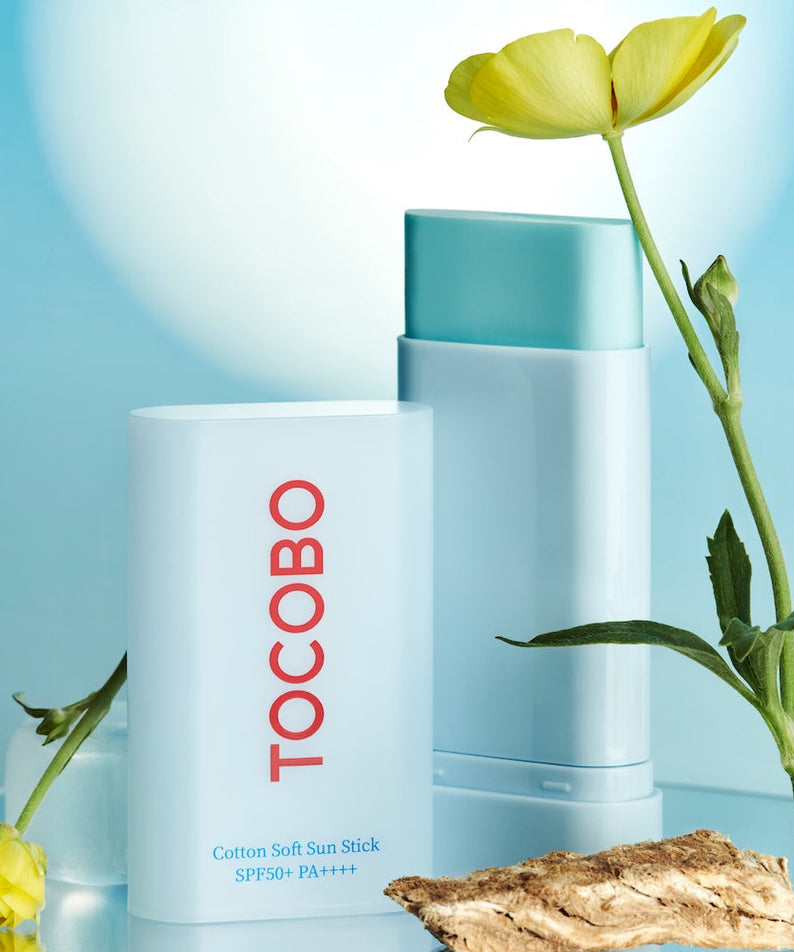TOCOBO  Cotton Soft Sun Stick, baume solaire coton, sur fond bleu clair avec fleurs et étui de produit