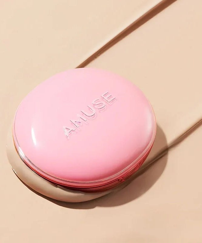 AMUSE Dew Power Vegan Cushion de AMUSE, coussin rose sur fond beige en studio, lumière douce et ombre.
