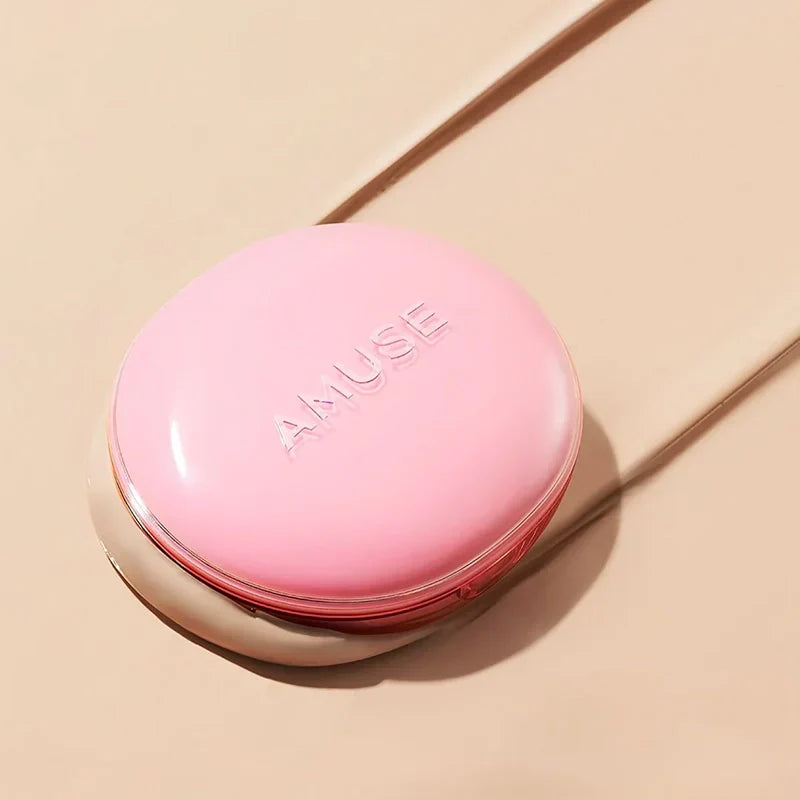 AMUSE Dew Power Vegan Cushion de AMUSE, coussin rose sur fond beige en studio, lumière douce et ombre.