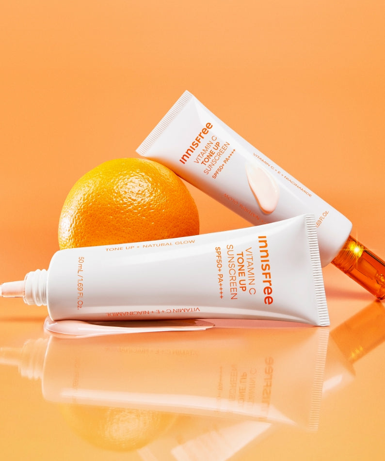 INNISFREE Vita C Spot Tone Up Sunscreen SPF50+/PA++++ 50ml, flacons et tube sur fond orange, agrumes et soleil