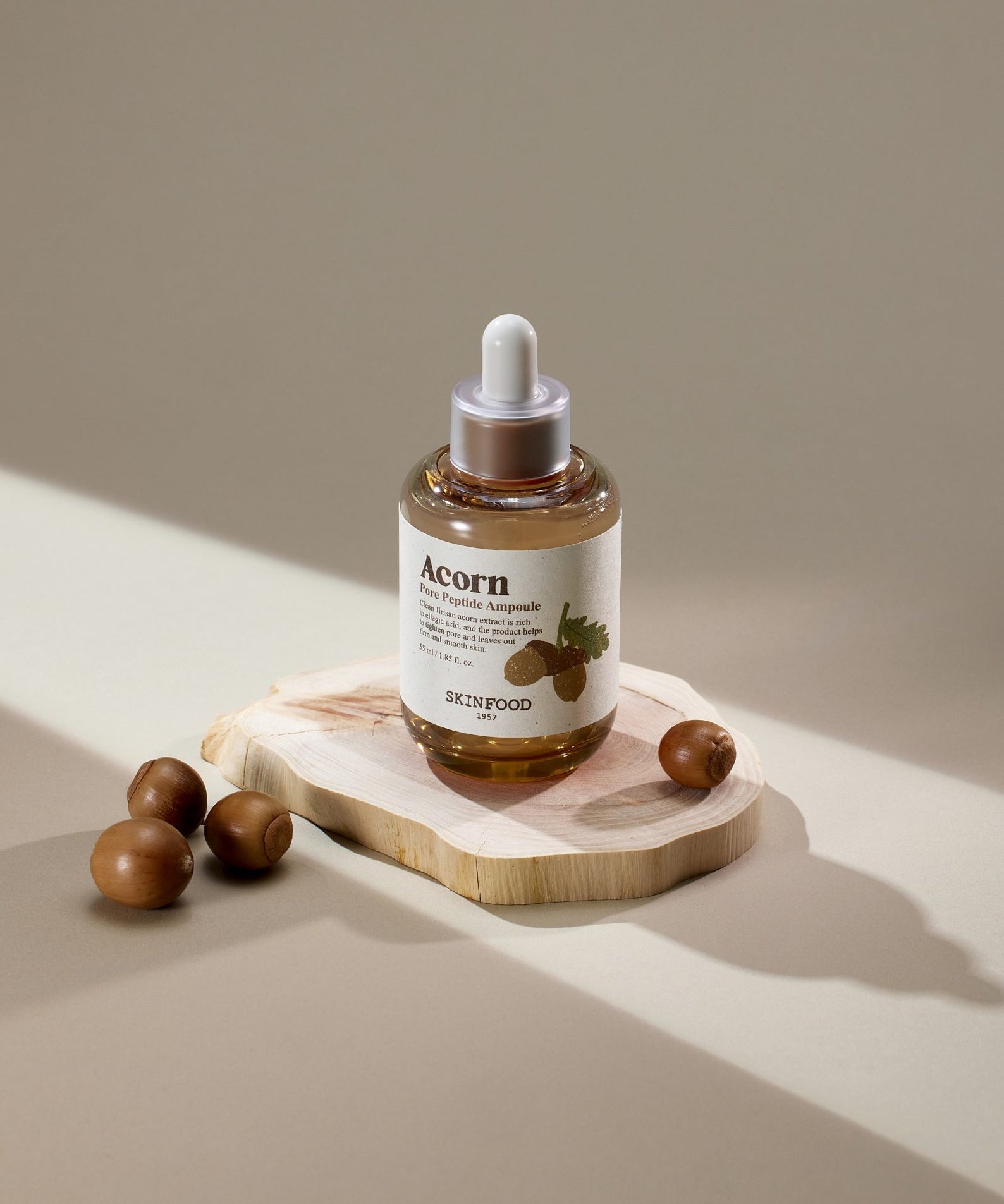 SKINFOOD Acorn Pore Peptide Ampoule 55ml, flacon SKINFOOD sur plateau bois avec billes d’acorn en studio.