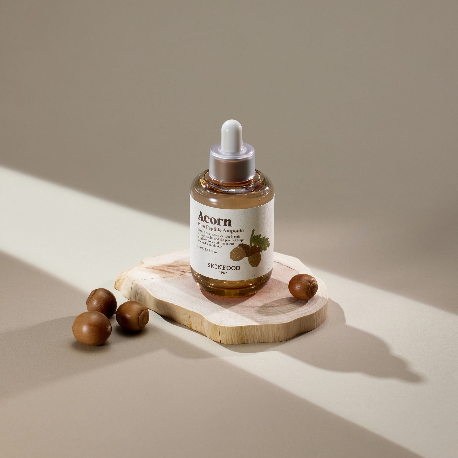SKINFOOD Acorn Pore Peptide Ampoule 55ml, flacon SKINFOOD sur plateau bois avec billes d’acorn en studio.