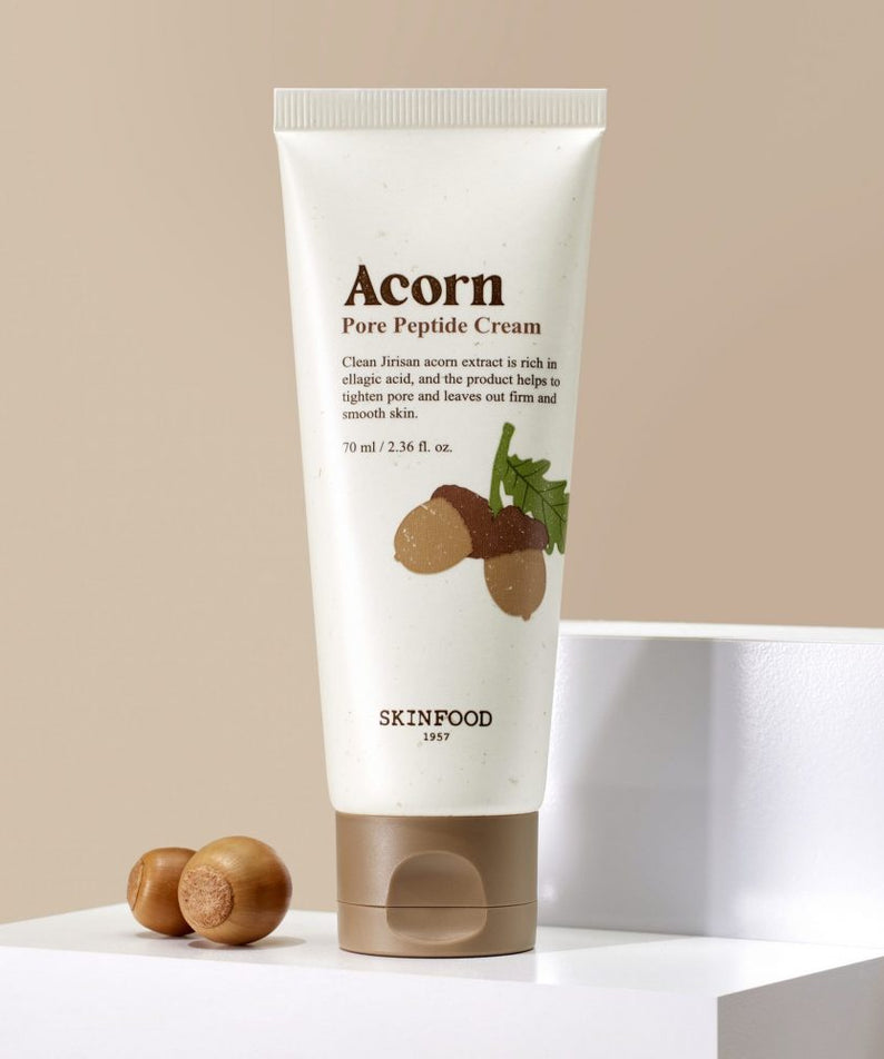 Décris l'image en français : SKINFOOD Acorn Pore Peptide Cleansing Foam 150ml, tube sur fond beige, contexte cosmétique.