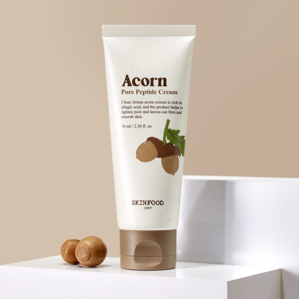 Décris l'image en français : SKINFOOD Acorn Pore Peptide Cleansing Foam 150ml, tube sur fond beige, contexte cosmétique.