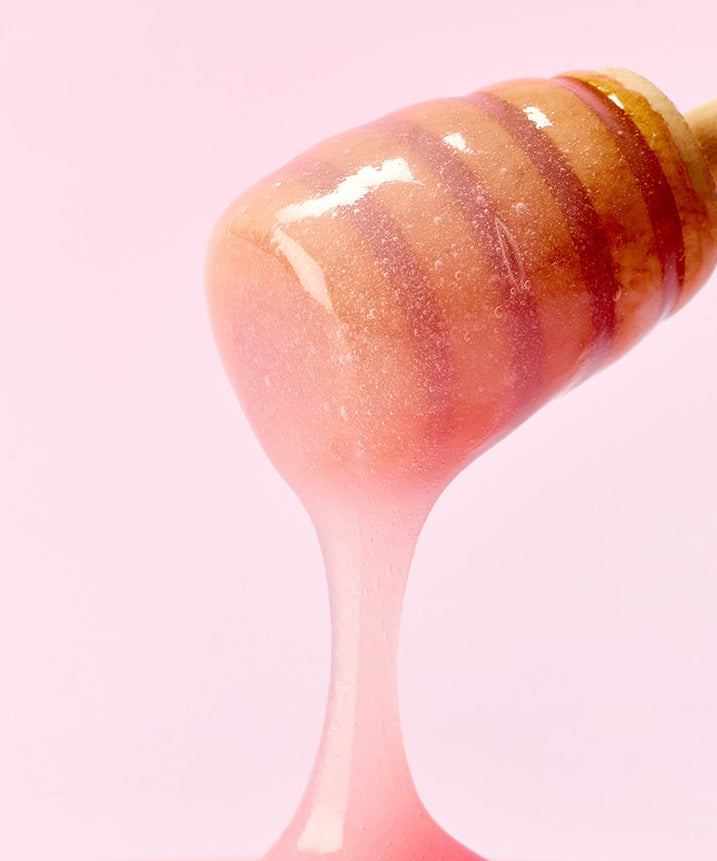 ARENCIA Honey Glazed Collagen Lip Mask 15g sur une cuillère en bois, texture miel étincelante, fond rose séduisant.