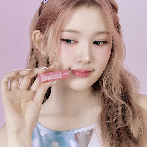 Décris l'image : 2AN Mini Glaze Bouncing Tint, la marque 2AN, maquillage lèvres rose sur fond violet avec jeune femme tenant le produit.