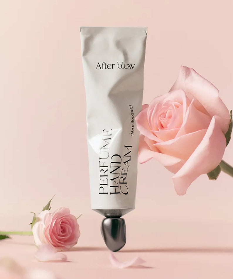 AFTER BLOW Perfume Hand Cream 50ml, main crème parfumée de la marque After blow, posée avec une rose et fleurs sur fond clair.