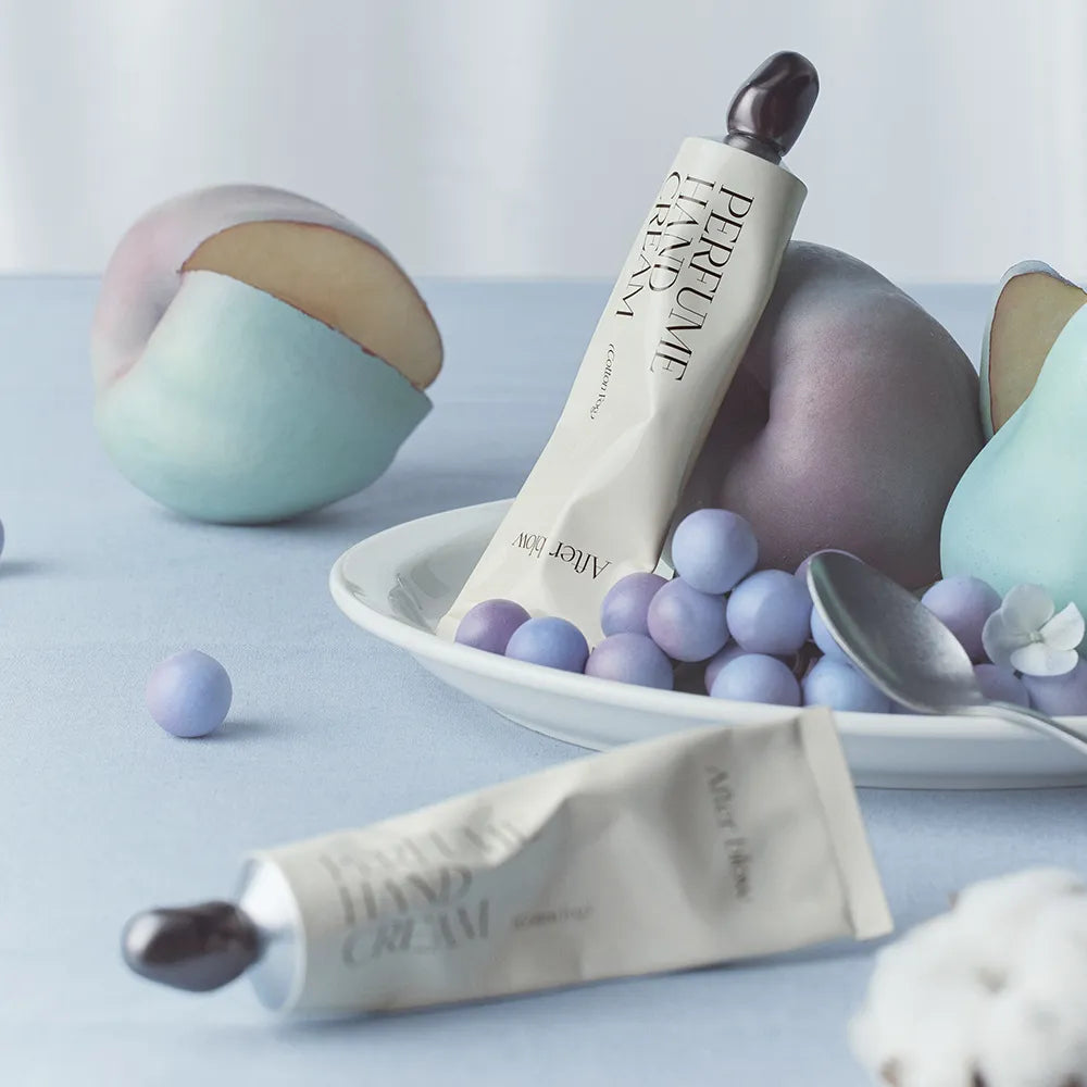 AFTER BLOW Perfume Hand Cream 50ml de la marque AFTER BLOW, tube sur fond pastel avec boules de cire et fleurs.