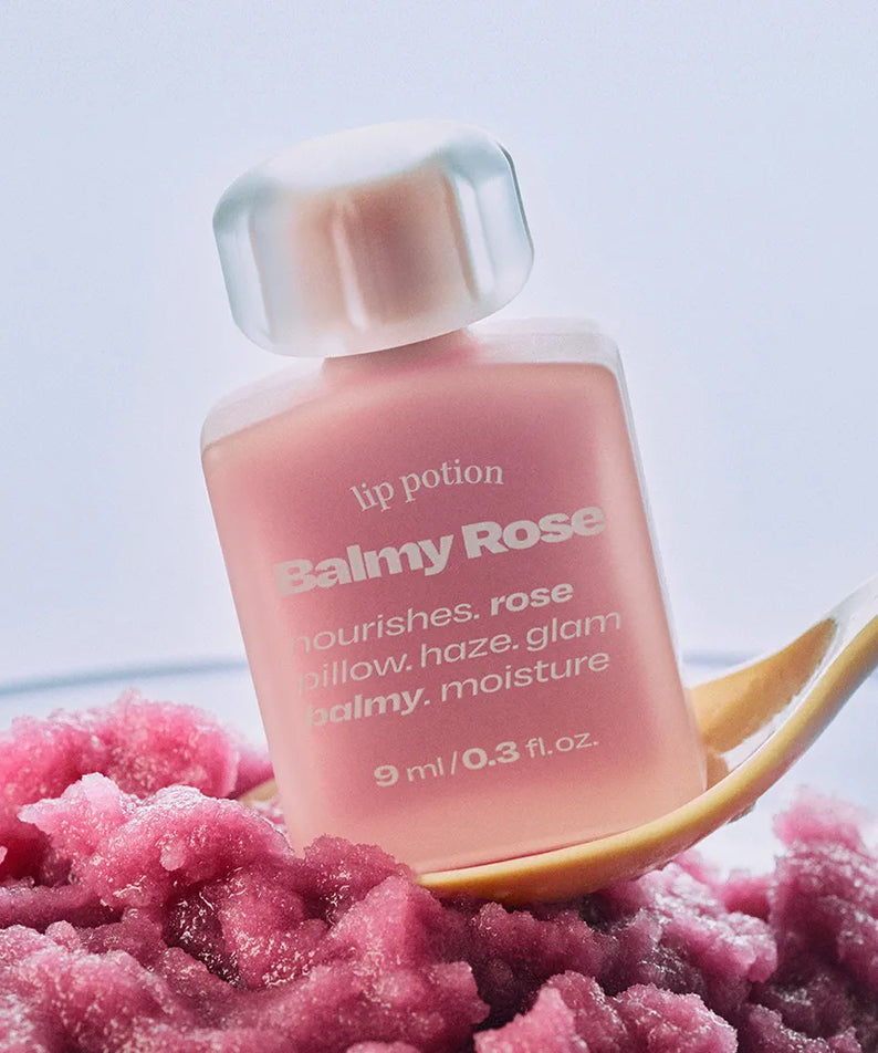 ALTERNATIVE STEREO Lip Potion Balmy Rose, baume lèvres rosé sur fond clair avec texture rose et cordon doré, studio.