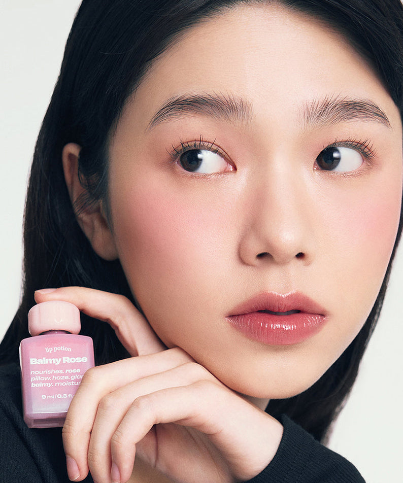 ALTERNATIVE STEREO Lip Potion Balmy Rose, baume rosé sur fond clair, femme tient le produit maquillage lèvres