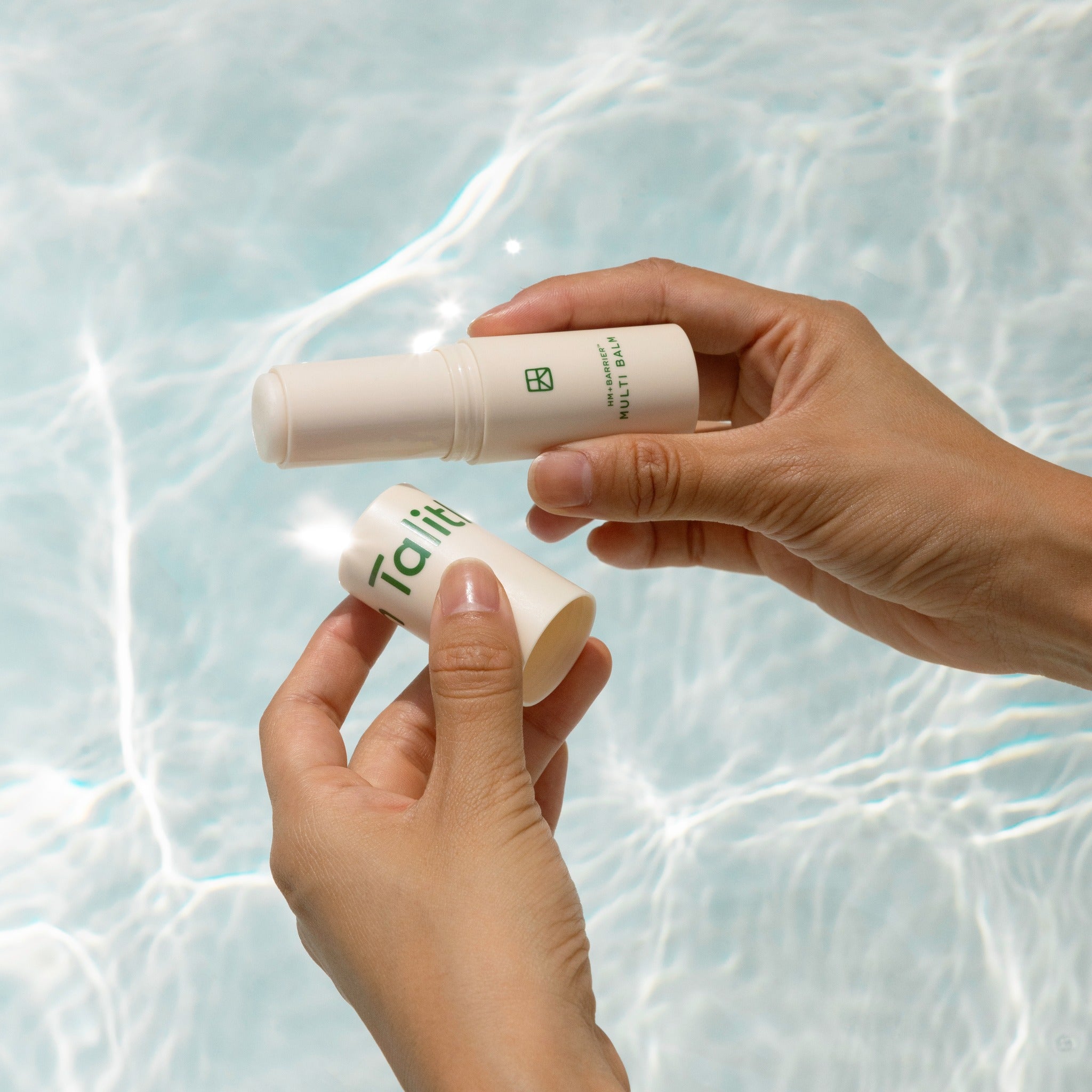 TALITHA KOUM HM+ Barrier Multi Balm 9g de Talitha, main applique un baume sur la peau devant fond aquatique