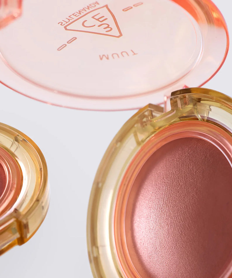 Gros plan sur 3CE Bouncy Blur Balm de 3CE, baume teinté dans son étui doré, texture rosée sur fond clair
