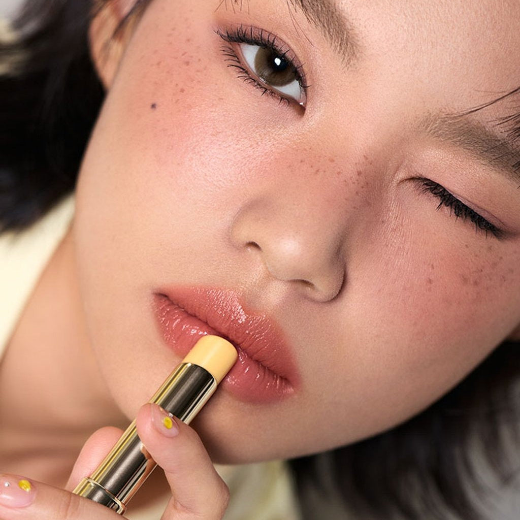 3CE Color Baker Glazy Lip Glow : femme applique un baume luisant sur lèvres, gros plan maquillage