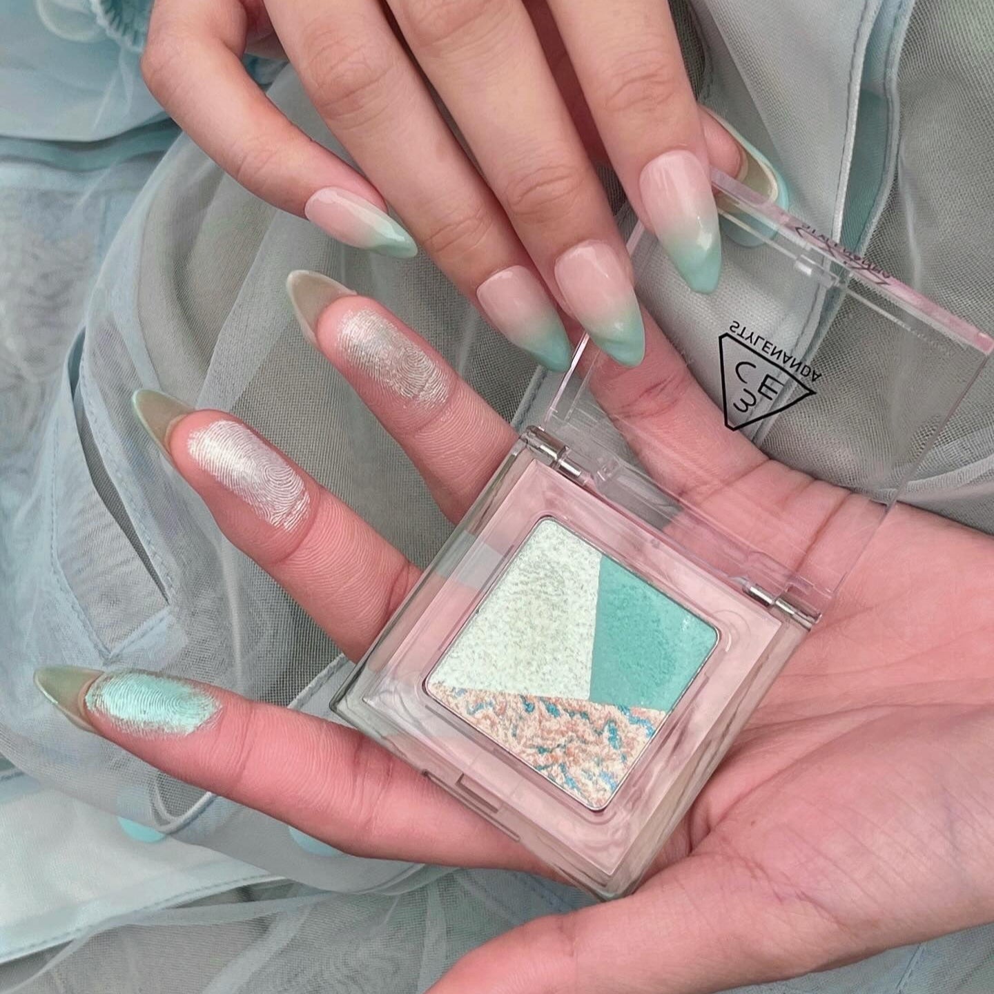 3CE Color Grid Eyeshadow de la marque 3CE, mains avec maquillage pastel et palette dans un style maquillage doux.