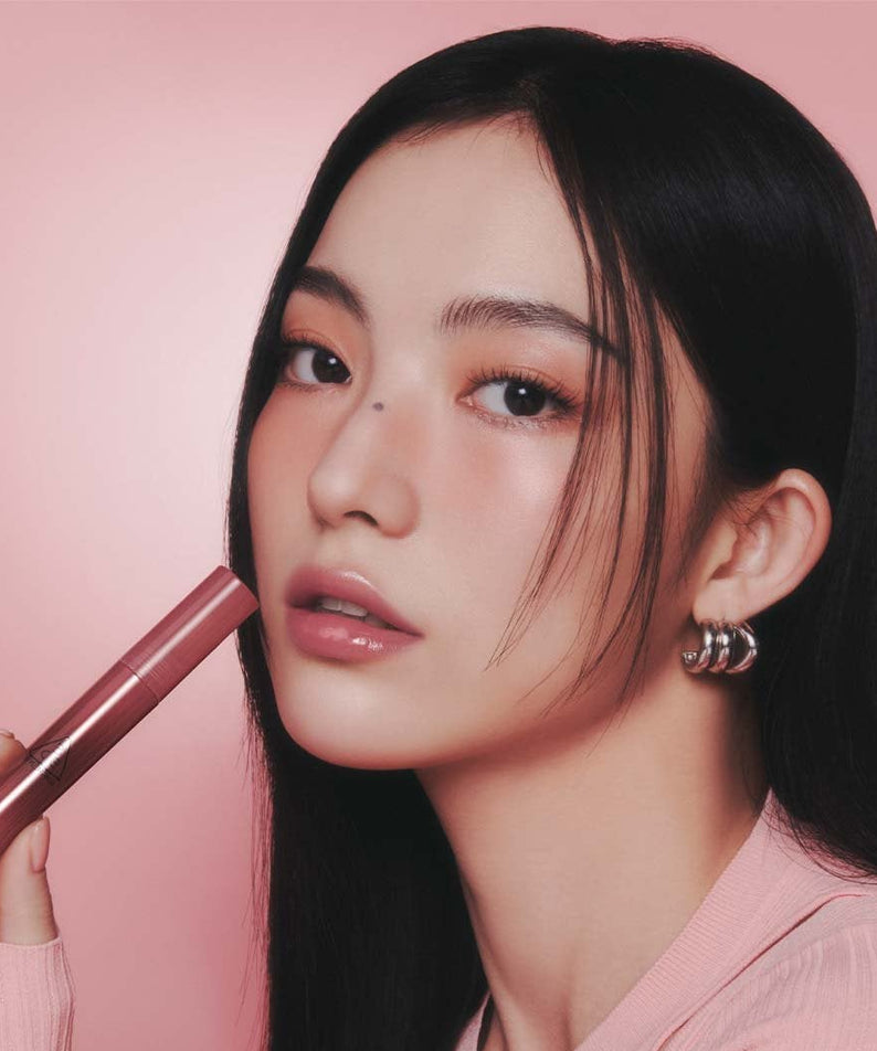 3CE Drop Glow Gel 10 Shades, la marque 3CE sur lèvres hydratées; femme maquillée tenant un baume, fond rose