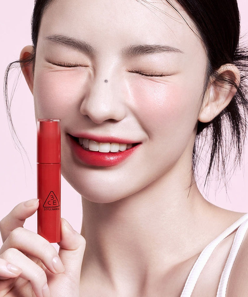 3CE Lazy Pop Lip Stain : la marque 3CE, maquillage sur lèvres rouges et main tenant le lip stain devant fond rose.