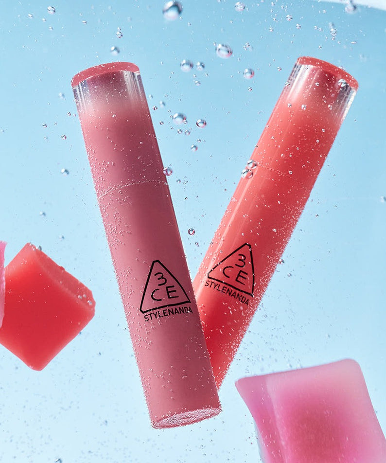 3CE Lazy Pop Lip Stain de StyleNANDA, tubes rouge rosé et bouchons en contexte éclaboussures d’eau sur fond bleu.