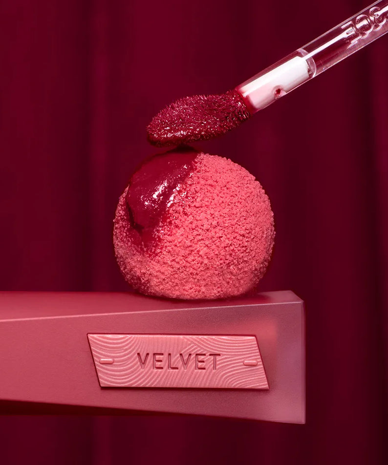 3CE Velvet Lip Tint Plush, rouge à lèvres dégradé sur étui rose et appliqué, fond bordeaux velours, photo produit.