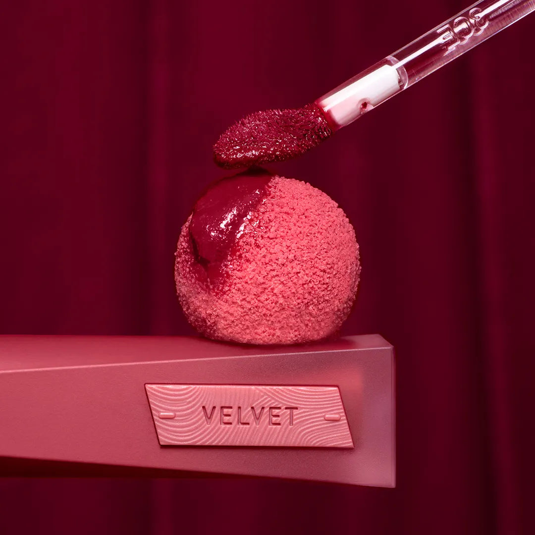 3CE Velvet Lip Tint Plush, rouge à lèvres dégradé sur étui rose et appliqué, fond bordeaux velours, photo produit.