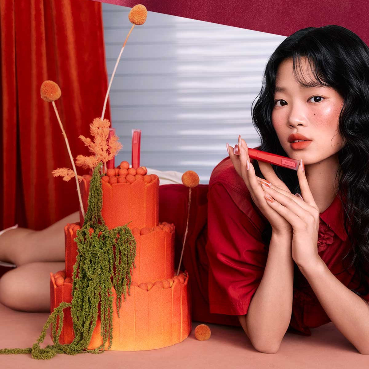 3CE Velvet Lip Tint Plush, femme maquillage lèvres rouges sur décor camaïeu rouge et orange, photo lifestyle.