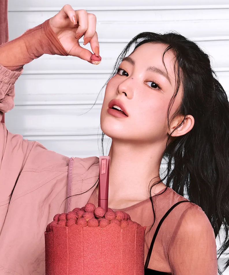 3CE Velvet Lip Tint Plush de 3CE, maquillage sur fond clair, appliqué sur les lèvres d’une jeune femme.