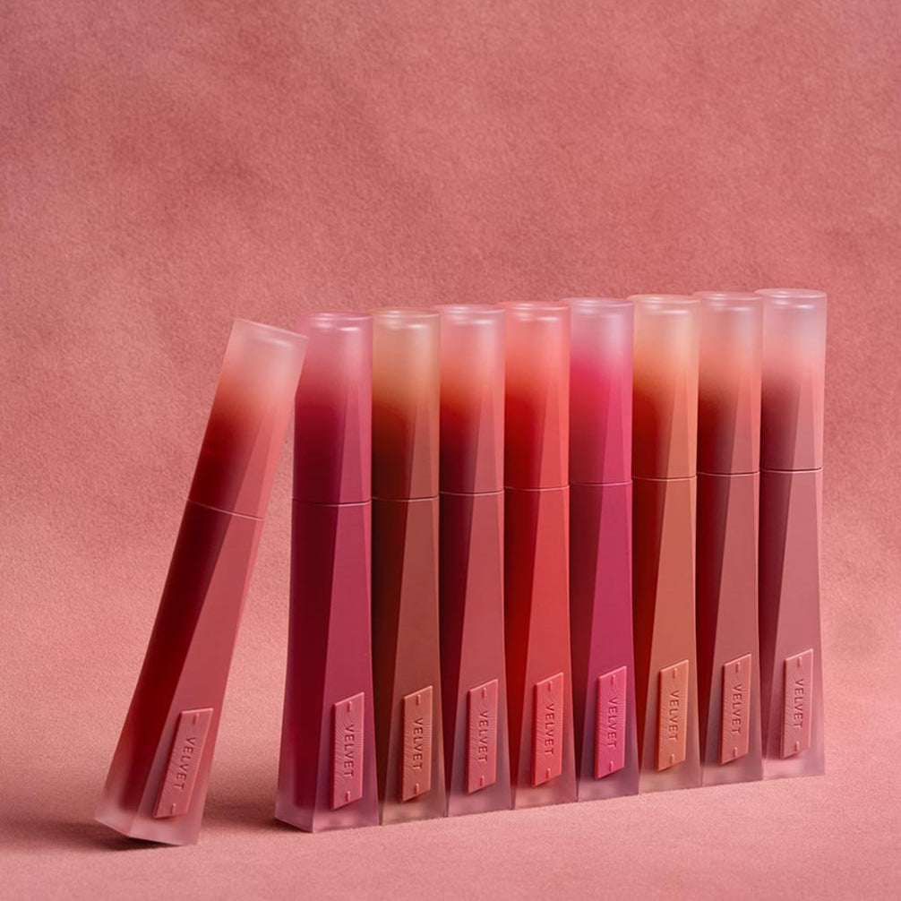 3CE Velvet Lip Tint Plush sur fond rose, rangée de tubes maquillage 3CE, rendu velouté et couleurs nude/rosées.