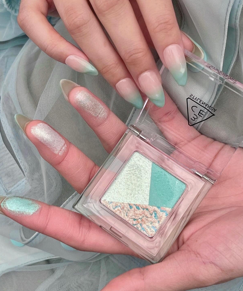 Palette 3CE Color Grid Eyeshadow aux teintes pastel vertes et bleues, mise en valeur par des mains élégantes.