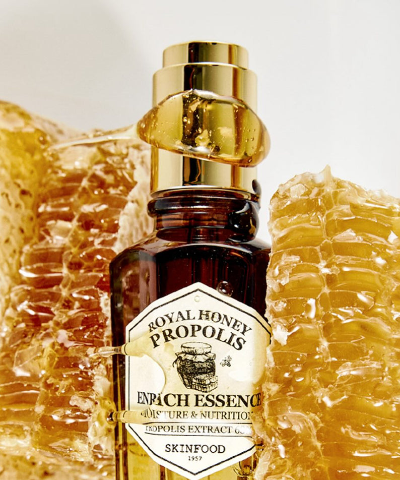 SKINFOOD Royal Honey Propolis Enrich Essence 50ml, flacon sur fond beige avec cire de miel et propolis, contexte visuel.