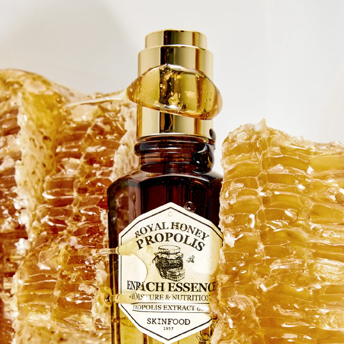 SKINFOOD Royal Honey Propolis Enrich Essence 50ml, flacon sur fond beige avec cire de miel et propolis, contexte visuel.