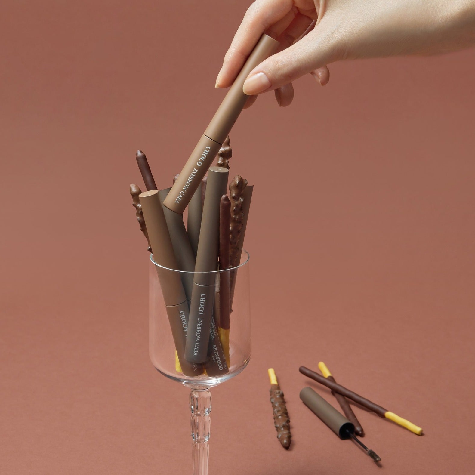 SKINFOOD Choco Eyebrow Cara, marque SkinFood, maquillage des sourcils : stylo applicateur tenu à la main sur fond beige