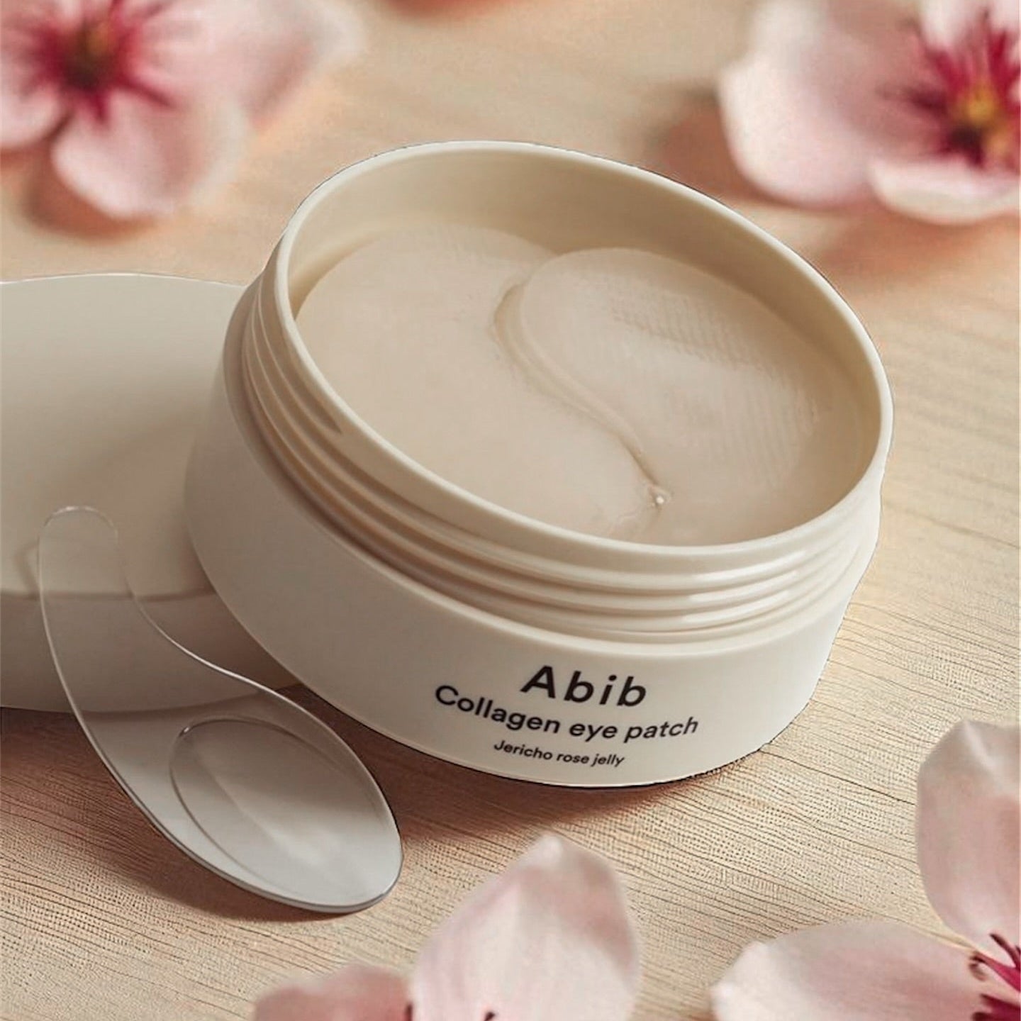 ABIB Collagen Eye Patch Jericho Rose Jelly 90g d’Abib, pot crème et patch sous fleurs roses, table beige.