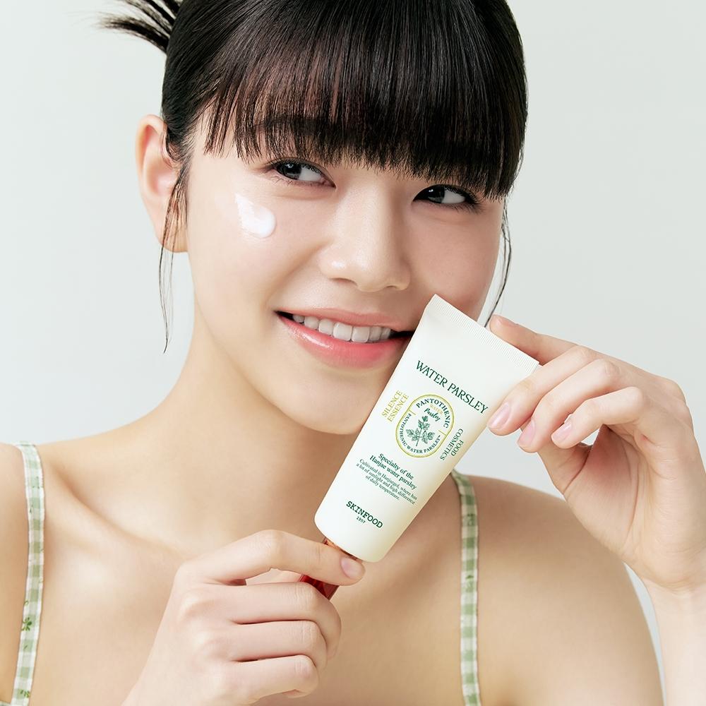 SKINFOOD Pantothenic Water Parsley Silence Essence 70ml, femme souriante applique le soin, fond clair, flacon vert.