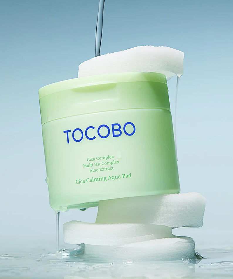 TOCOBO Cica Calming Aqua Pads 60p 160ml : pot vert TOCOBO sur coussins blancs, ambiance spa, gouttes d’eau.