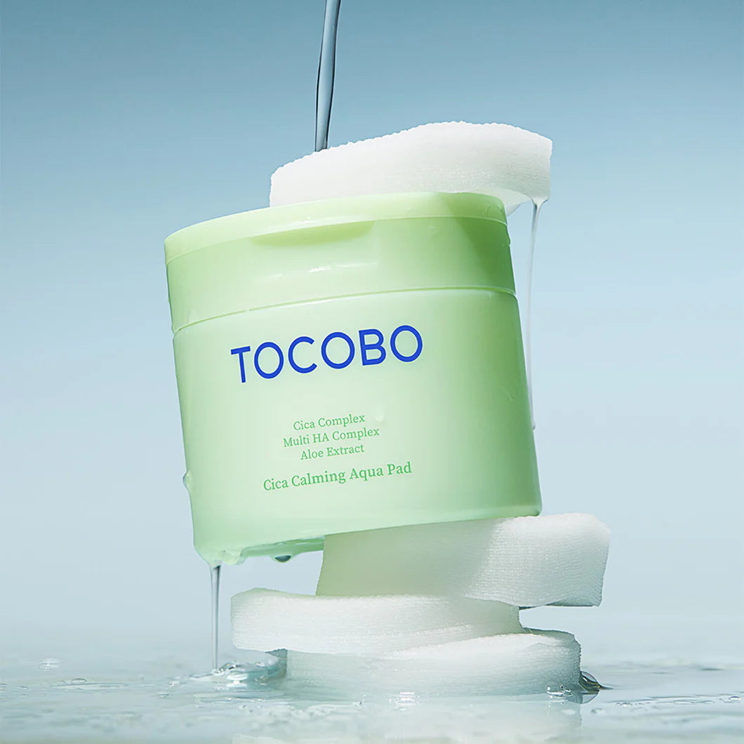 TOCOBO Cica Calming Aqua Pads 60p 160ml : pot vert TOCOBO sur coussins blancs, ambiance spa, gouttes d’eau.