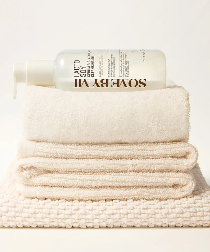SOME BY MI Lacto Soy Serum & Blackhead Cleansing Oil 200ml, flacon sur serviettes, style minimaliste blanc.
