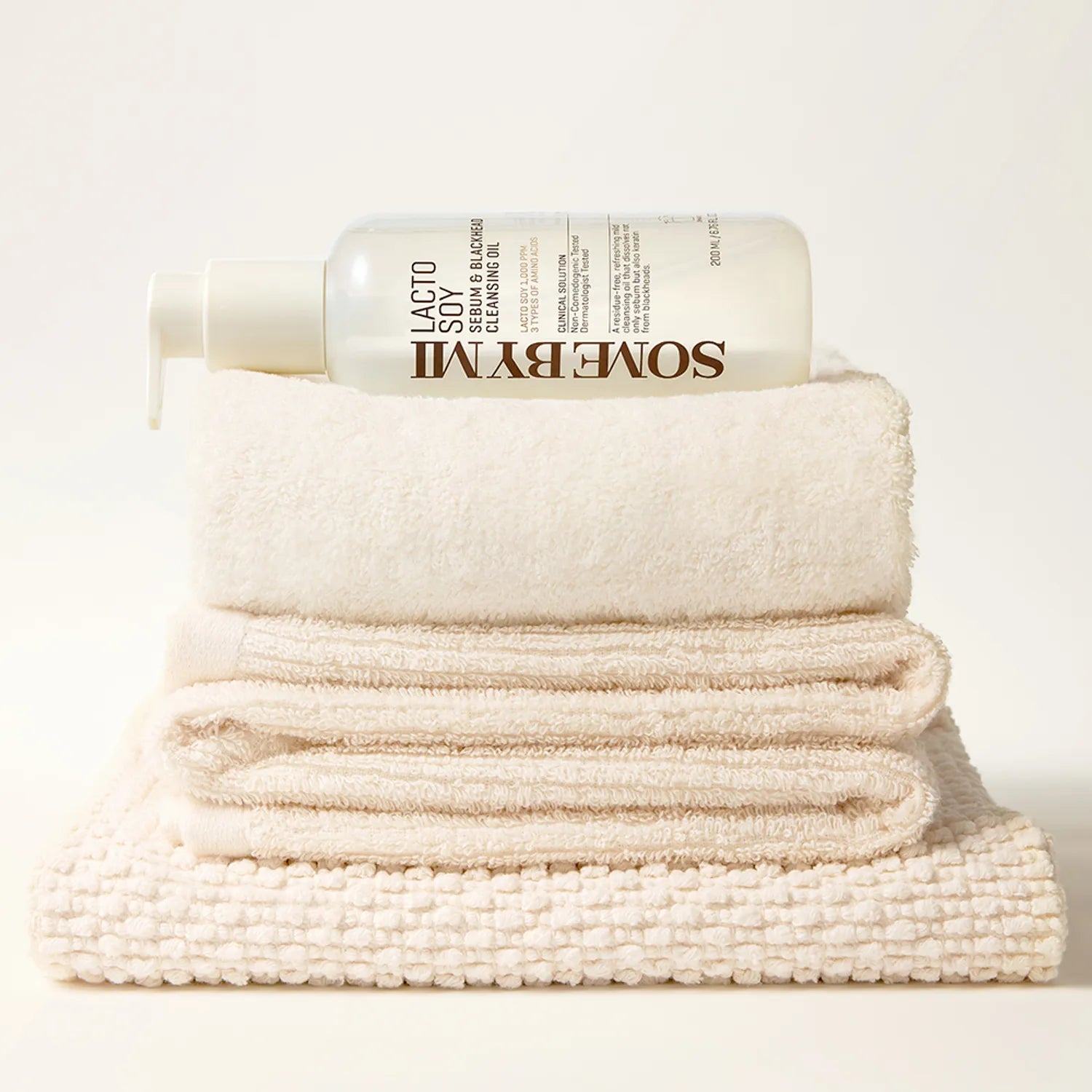 SOME BY MI Lacto Soy Serum & Blackhead Cleansing Oil 200ml, flacon sur serviettes, style minimaliste blanc.