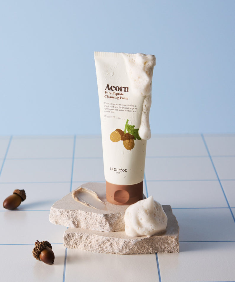 SKINFOOD Acorn Pore Peptide Cleansing Foam 150ml sur fond bleu avec mousse, éclats de pierre et noisettes
